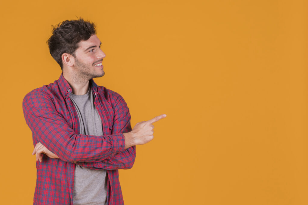 smiling-portrait-young-man-pointing-his-finger-against-orange-backdrop